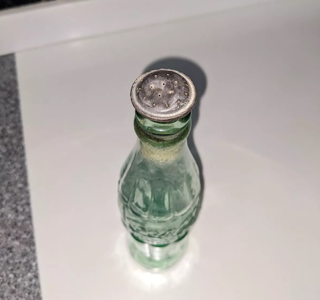 The vintage glass sprinkler bottle with its cap securely fitted, emphasizing its historical charm and practicality in household chores