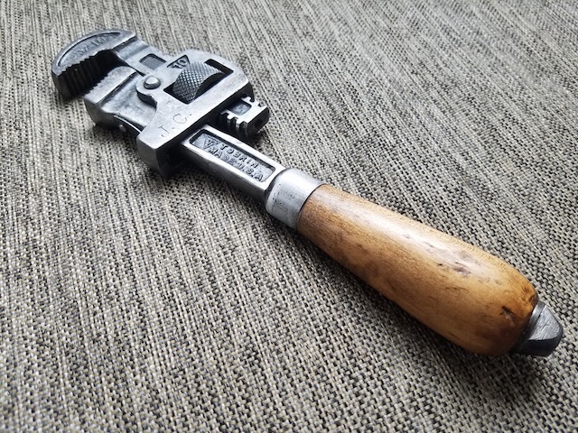 A well-preserved example of a vintage Stillson wrench, showcasing the smooth wooden handle that provided a comfortable grip for users over the years