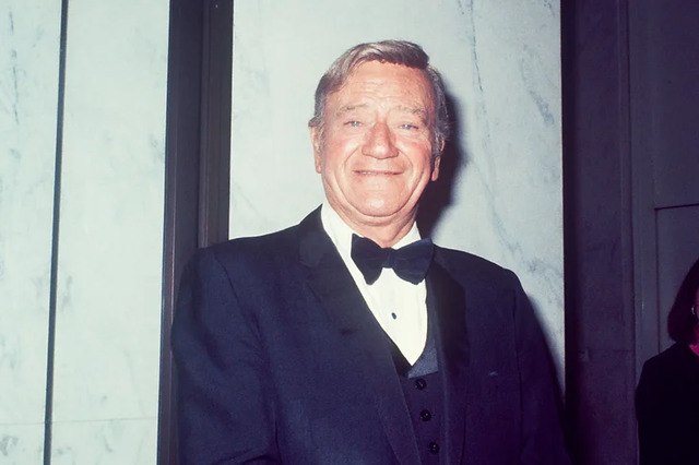 A smiling John Wayne in formal attire, epitomizing his status as a cinematic legend.