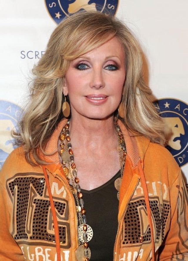 A chic and stylish Morgan Fairchild at a public appearance, sporting a trendy and casual orange hoodie, yet still radiating the glamour of her Hollywood days