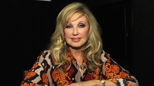 Morgan Fairchild attending an event in a bold animal print outfit, her beauty still glowing as she confidently sits for the camera, exuding her enduring elegance