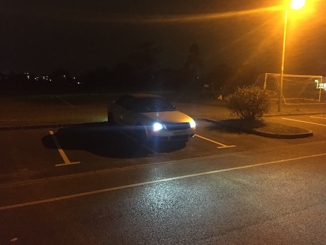 A vehicle with powerful LED headlights standing out in a dimly lit parking area