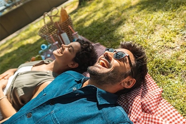 Two people lying on the grass with radiant smiles, embodying the carefree happiness of a perfectly planned outdoor date