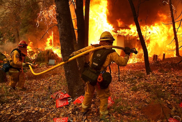 Firefighters wielding hoses while battling the fierce flames of a wildfire, risking their lives to prevent the fire's spread