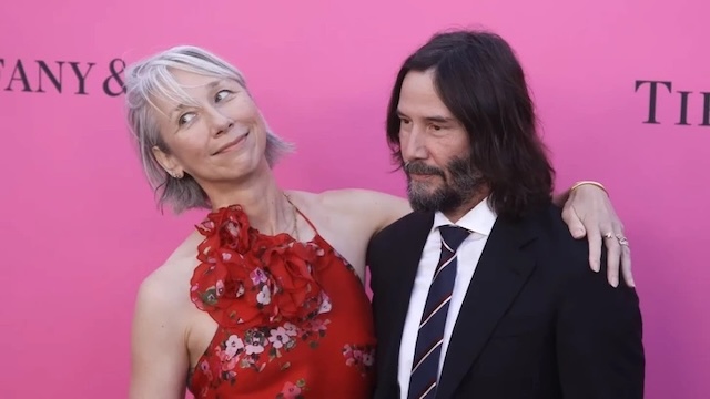 A loving moment captured between Keanu Reeves and Alexandra Grant at a high-profile event, sharing a glance of admiration