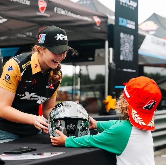 Kayla Yaakov sharing a special moment with a young fan, signing a helmet and inspiring the next generation of racers