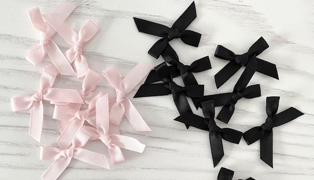 A collection of tiny satin bows in black and pink, ready to be stitched onto garments, representing the roots of this design feature