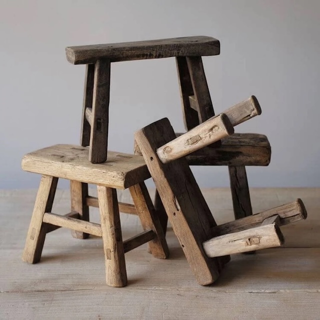 A stack of several traditional wooden milking stools, showcasing the variety of designs and their sturdy, utilitarian build