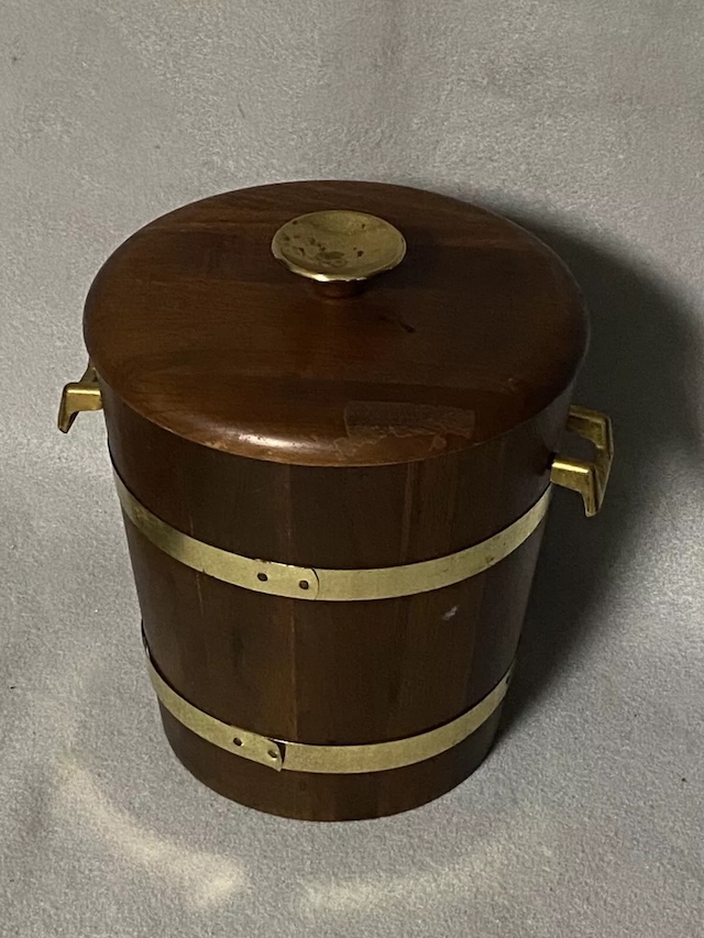 This vintage ice bucket captures the timeless charm of the past, featuring a sturdy wooden body with polished brass accents.