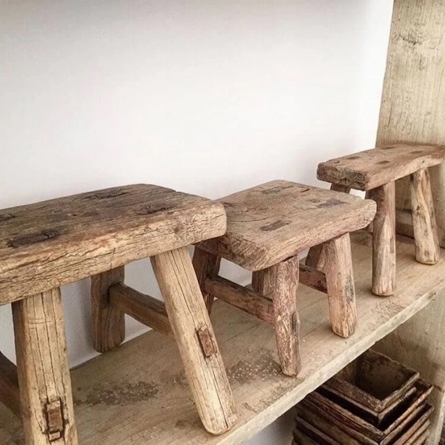 A lineup of three neatly arranged traditional wooden milking stools on a wooden shelf, highlighting their timeless design and practicality