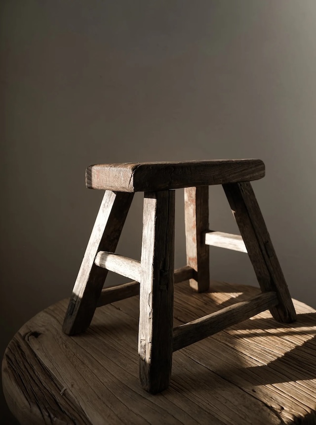 A beautifully lit portrait of a traditional wooden milking stool, capturing the texture of the wood and its nostalgic charm in soft, warm light