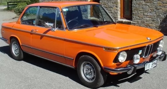 A vibrant orange BMW 2002 Tii stands out with its classic rally-style front fog lights, capturing the car's sporting spirit and performance-oriented design