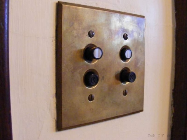 Another perspective of a push-button light switch against a wall, showing its sturdy brass construction and timeless functionality