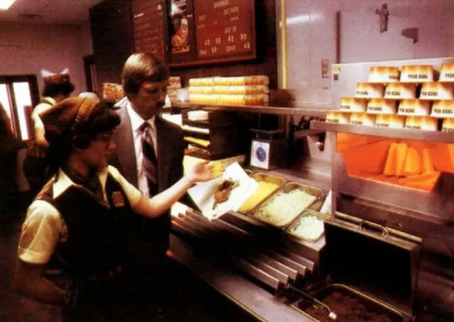 A 1970s photo showing a Taco Bell employee happily serving food to a customer, highlighting the fast, friendly service that Taco Bell became known for.