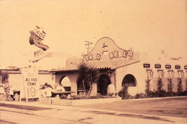 A classic photo of Taco Bell’s first-ever restaurant on Firestone Boulevard in Downey, California. The charming vintage design captures the early days of the beloved fast food chain.