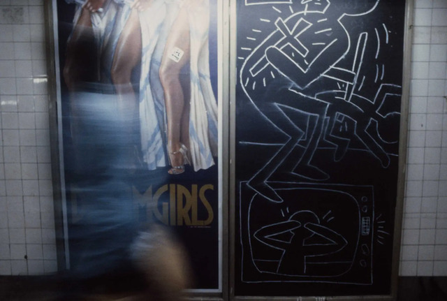 A commuter walks past a “Dreamgirls” poster and a striking chalk drawing by Keith Haring, merging the worlds of music and street art in 1981.