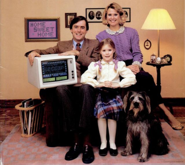 A family sits together with a computer system, reinforcing the idea of home computers becoming an integral part of family life in the 1980s.