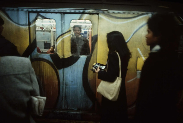 A woman stands, waiting for her train to arrive, as graffiti-covered subway cars, often more intricate on the outside, roll in.