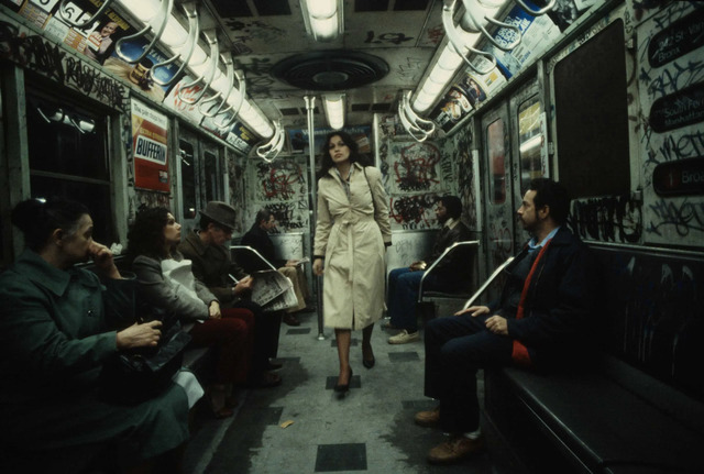 Captured in 1981 by Christopher Morris, a woman strolls through a subway car covered in vibrant graffiti, reflecting the urban art that dominated the era.