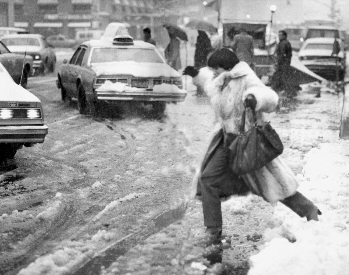 A daring pedestrian leaps over a towering snow mound into the bustling streets of New York City, 1982.