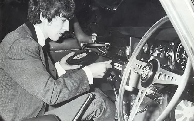 George Harrison proudly displays the Philips Auto Mignon turntable inside his elegant 1965 Jaguar XKE.