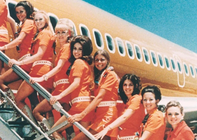 Several stewardesses stand in line, ready for a photo. They smile as they pose together