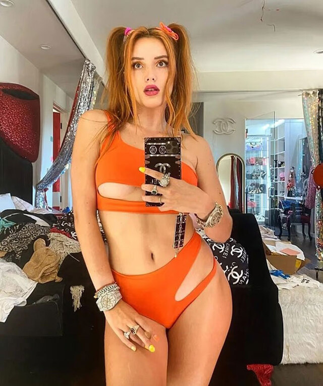 Bella Thorne capturing a bold mirror selfie in her bedroom, with piles of clothes and décor creating a chaotic backdrop.
