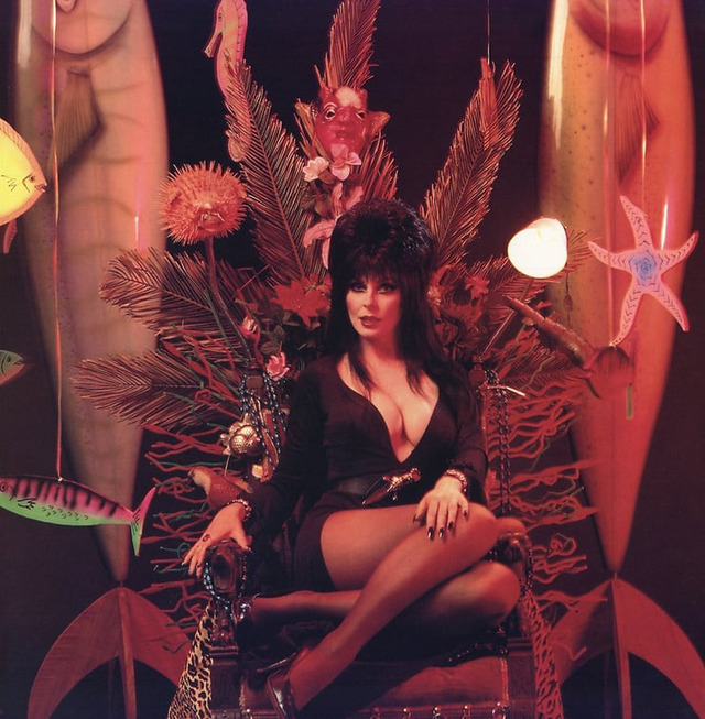 Elvira sitting on a throne of oddities, embodying her mix of humor, camp, and gothic flair.