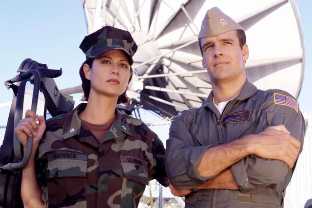 Standing side by side in military fatigues, Catherine Bell and David James Elliott embody the partnership and tension that kept audiences hooked throughout the series.