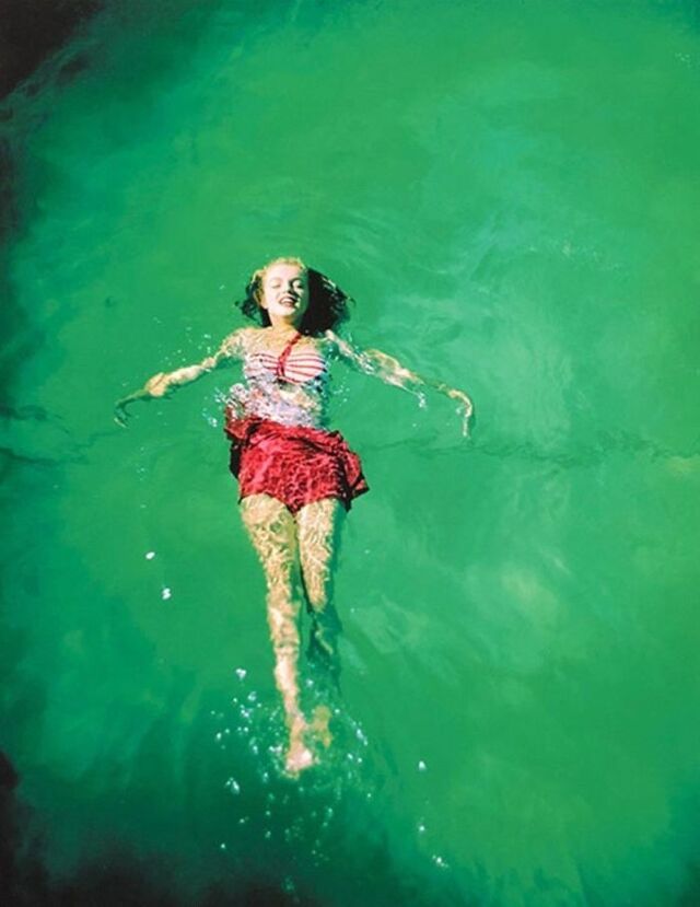 A young Norma Jeane floating effortlessly in clear green water during one of her earliest outdoor photoshoots, radiating calmness and natural charm.