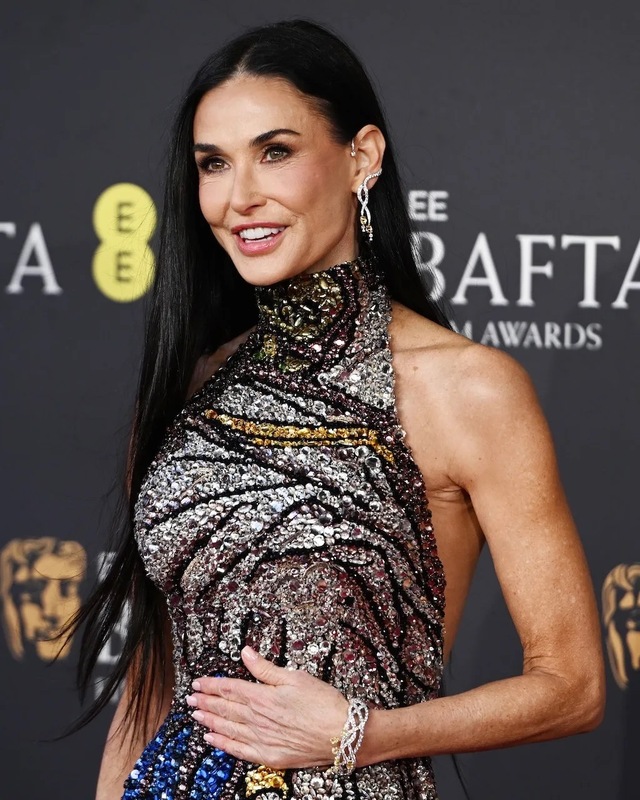 Clad in a high-neck, backless silver gown that shimmered under the lights, Demi Moore effortlessly combined classic Hollywood glamour with a bold modern twist.
