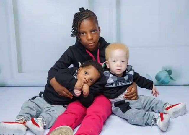 Older sister Demilade embraces her two younger brothers, Daniel and David, showing the strong sibling connection that transcends appearances.