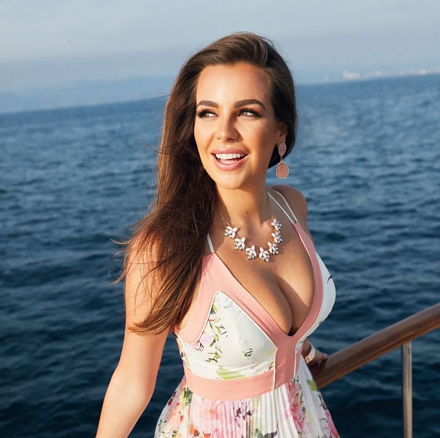 Penny Lane smiling radiantly in a floral dress, her presence complementing the beautiful oceanic background.